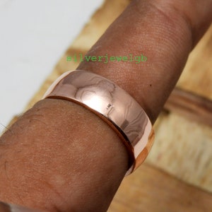 May include: A wide rose gold band ring worn on a finger.