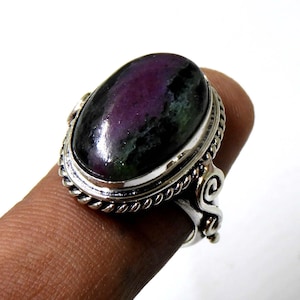 Könnte beinhalten: Ein silberner Ring mit einem ovalen, grün-violetten Edelstein, der in einem dekorativen Silberband gefasst ist.