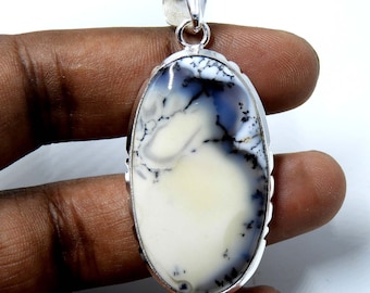 Pode incluir: Um pingente de prata com uma pedra de opala dendrítica branca e cinza. A pedra de forma oval tem um padrão único de dendritos pretos. O pingente é engastado em uma moldura de prata com uma borda detalhada.