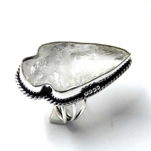 Op de afbeelding: Een zilveren ring met een heldere kwarts pijlpuntvormige steen. De ring heeft een gevlochten band en een parelrand.