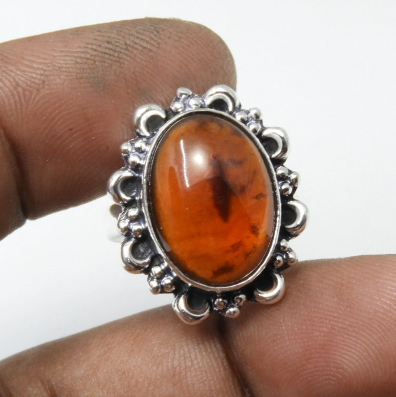 May include: A silver ring with an oval-shaped amber gemstone set in a decorative filigree design.