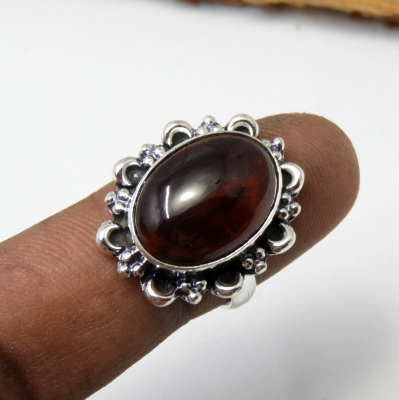 May include: A silver ring with an oval-shaped, dark brown gemstone set in a decorative, floral-patterned bezel.