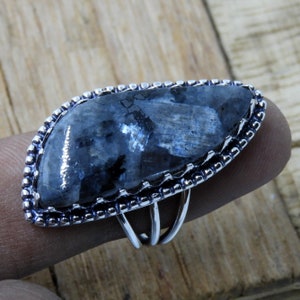 May include: A silver ring with a large, dark blue, iridescent gemstone set in a silver bezel. The ring has a delicate, ornate design.