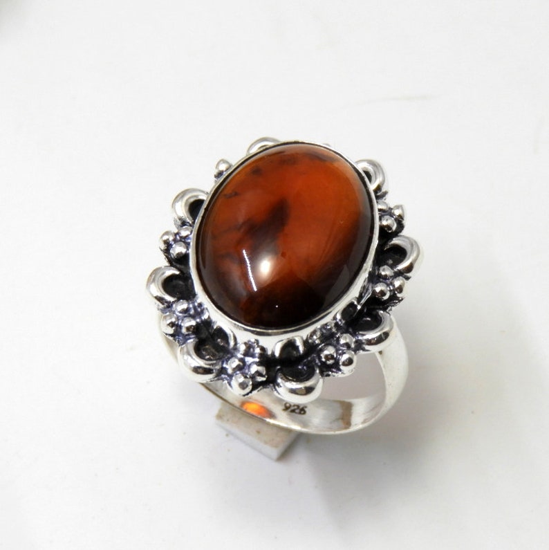 May include: A silver ring with an oval-shaped brown gemstone set in a decorative floral design. The ring is marked "925" on the band.