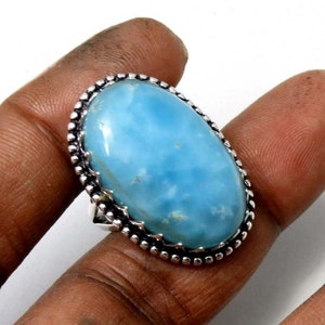May include: A silver ring with a large oval blue gemstone. The ring has a decorative border around the stone.