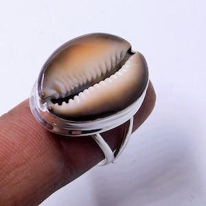 Op de afbeelding: Een zilveren ring met een bruine en witte kauri schelp in het midden.