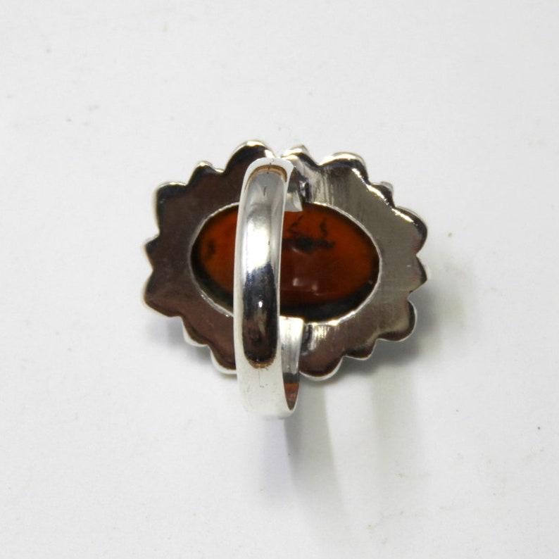 May include: A silver ring with an oval-shaped amber stone set in a decorative silver bezel. The ring is shown from the back, revealing the smooth silver band.