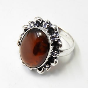 May include: A silver ring with an oval-shaped amber stone set in a detailed floral design.