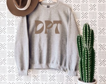 May include: A gray sweatshirt with the word "DPT" printed in brown on the front. The sweatshirt is hanging on a wooden hanger against a white background with a black geometric pattern. A brown hat and a potted cactus are also visible in the image.