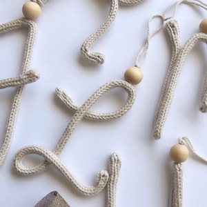 May include: A set of knitted letters with wooden beads, spelling out the word "Love". The letters are beige and the beads are natural wood.