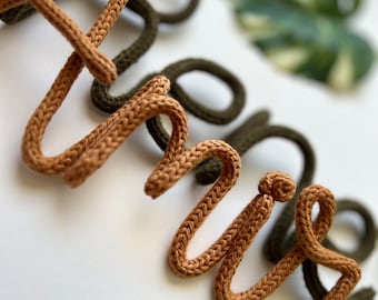 May include: The word "hello" spelled out in brown and green yarn. The yarn is woven in a knit stitch. The letters are on a white background with green and white leaves.