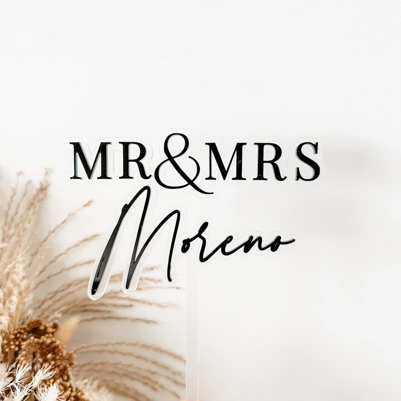 May include: A clear acrylic cake topper with black text that reads "MR & MRS Moreno".