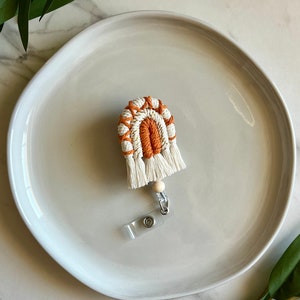 May include: A white and orange crocheted rainbow keychain with a white bead and a clear plastic badge holder.