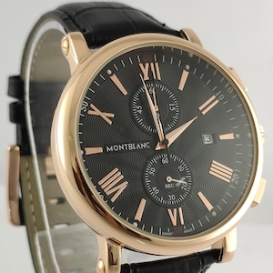 May include: A luxury wristwatch with a black face, rose gold accents, and a black leather strap. The watch face features Roman numerals and the brand name "MONTBLANC". The watch has a date display and multiple sub-dials.