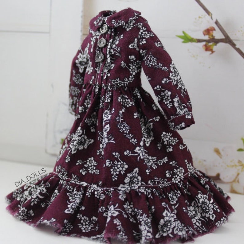 May include: A burgundy dress with a white floral pattern and a ruffled hem. The dress has a collared neckline and long sleeves.