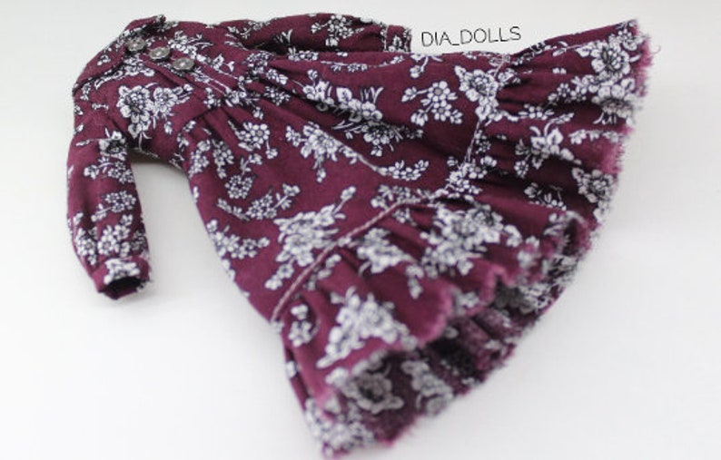 May include: A burgundy dress with a white floral print and a ruffled hem. The dress has long sleeves and a button-up front.