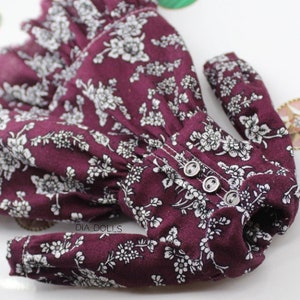 May include: A burgundy dress with white floral print and long sleeves. The dress has three buttons down the front.