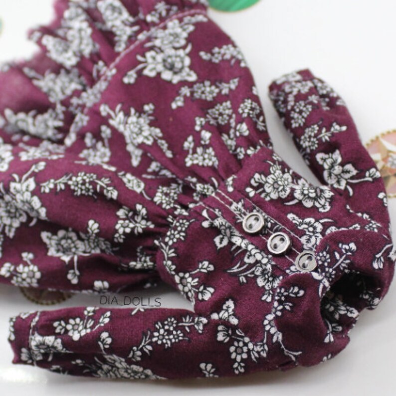 May include: A burgundy dress with white floral print and long sleeves. The dress has three buttons down the front.