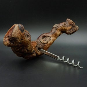 Può includere: Un cavatappi in legno con una finitura marrone naturale e una spirale in metallo argentato. Il cavatappi ha la forma di un ramo curvo.