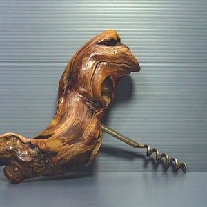 Può includere: Un cavatappi in legno con una finitura marrone naturale. Il cavatappi ha la forma di una testa di uccello e ha una spirale di metallo.