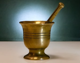May include: A brass mortar and pestle with a smooth, polished finish. The mortar has a wide, round base and a tall, cylindrical pestle.
