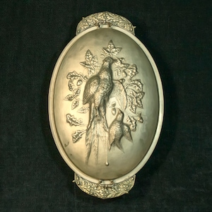 May include: An oval silver-toned metal box with a relief of two birds on a branch with leaves and acorns. The box has ornate floral trim and a clasp. The design is highly detailed.