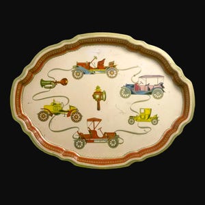 Peut inclure: Plateau de service ovale vintage avec un fond crème et une bordure décorative. Le plateau présente des illustrations colorées de voitures anciennes, d'un klaxon et d'une lanterne. La bordure est rouge et verte.