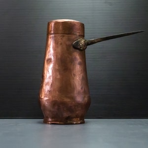 Peut inclure: Une cafetière en cuivre avec un bec long et fin. La cafetière a une finition martelée et une poignée décorative.