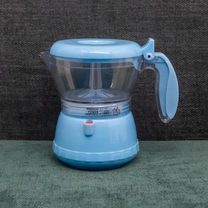 Puede incluir: Una cafetera eléctrica azul claro con una cámara superior transparente y clara. La cafetera tiene un asa, un botón de encendido rojo y el texto "MEDIUM POWER (MAX 110°C)".