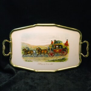 May include: A gold-rimmed serving tray with a white porcelain insert featuring a vintage illustration of a horse-drawn carriage with four horses and passengers. The text "Setting up to be shot" is printed below the image.