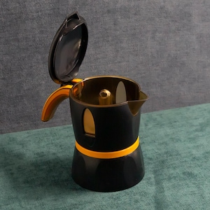 May include: A black and yellow stovetop espresso maker with the lid open. The coffee pot has a yellow handle and a yellow band around the base. The interior is a gold color. The coffee maker is sitting on a teal surface.
