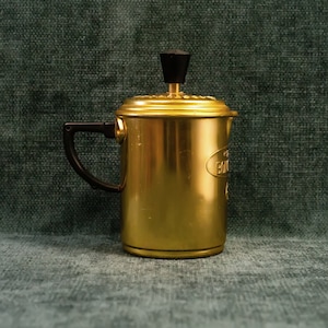 May include: A gold-coloured metal coffee maker with a black plastic lid and handle. The coffee maker has a label that reads "BIALETTI".