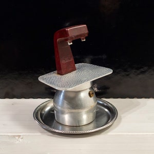 May include: A silver and white stovetop espresso maker with a red plastic handle. The maker is sitting on a silver tray.