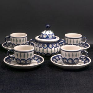 May include: A ceramic tea set with a sugar bowl and four teacups with saucers. The set features a white base with blue and green circular and leaf patterns. The sugar bowl has a lid with a blue knob. The teacups have small handles.