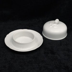以下が含まれることがあります： 蓋付きの白い磁器製のバター入れ。蓋には浮き彫りの花柄が施されています。