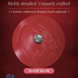 Op de afbeelding: Rode, ronde knop met een reliëf drakenontwerp en een kleine zilveren knop in het midden. De tekst luidt: "Een symbool van macht. Rijk gedetailleerd. Uniek vervaardigd. Aangepaste reliëf drakenknop upgrade." Het woord "STAUB" is ook zichtbaar.