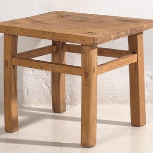 May include: A square, wooden side table with a natural finish. The table has four sturdy legs and a simple, rustic design. The table is approximately 18 inches tall and 18 inches wide.