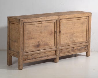 Peut inclure: Un buffet en bois brun clair avec deux portes et deux tiroirs. Le meuble est de forme rectangulaire et est fait de bois vieilli. Les portes ont de petites poignées rondes en métal. C'est un meuble.