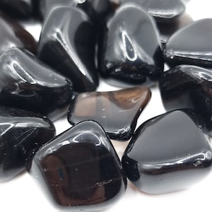 Peut inclure: Un ensemble de pierres d'obsidienne noire polies. Les pierres ont une surface lisse et brillante et varient en taille et en forme. La couleur sombre et la qualité réfléchissante des pierres ressortent sur le fond blanc.