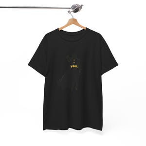 Könnte beinhalten: Schwarzes T-Shirt mit einer goldenen Silhouette einer Figur und den Worten "I AM THE VOID" in Gold. Das T-Shirt hängt an einem Holzbügel.