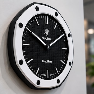 Könnte beinhalten: Eine schwarz-weiße Wanduhr mit geometrischem Design. Das Zifferblatt ist schwarz mit weißen Zeigern und Stundenmarkierungen. Der Text "AP x Swatch" und "Royal Pop" ist sichtbar. Die Uhr hat einen Durchmesser von etwa 30 cm.
