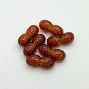 May include: A group of six brown glass beads, each bead is made of two connected oval shapes. The beads have a striated pattern.
