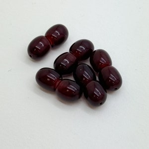 May include: A group of eight dark red oval-shaped beads. The beads are smooth and glossy.