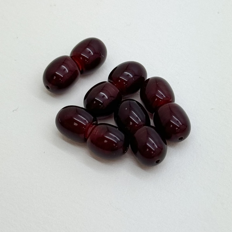 May include: A group of eight dark red oval-shaped beads. The beads are smooth and glossy.