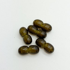 May include: Six brown, double-ended, glass beads with a textured surface. The beads are oval shaped and have a slightly darker brown color on one end.