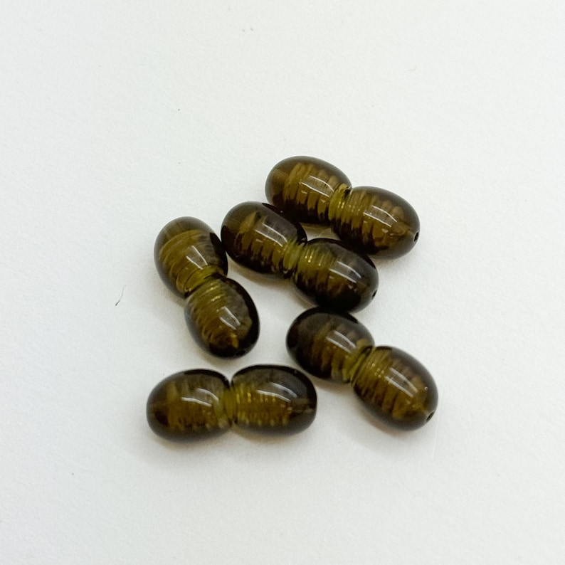 May include: Six brown, double-ended, glass beads with a textured surface. The beads are oval shaped and have a slightly darker brown color on one end.