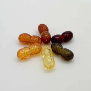 May include: A collection of six amber beads, each with a unique color and pattern. The beads are strung together in a circular shape, creating a decorative element.
