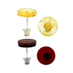 May include: Stud earrings with a silver post and backing. One pair features a yellow, translucent, circular top with gold flecks. The other pair has a dark brown, translucent, circular top. Both pairs are shown from the side and top.