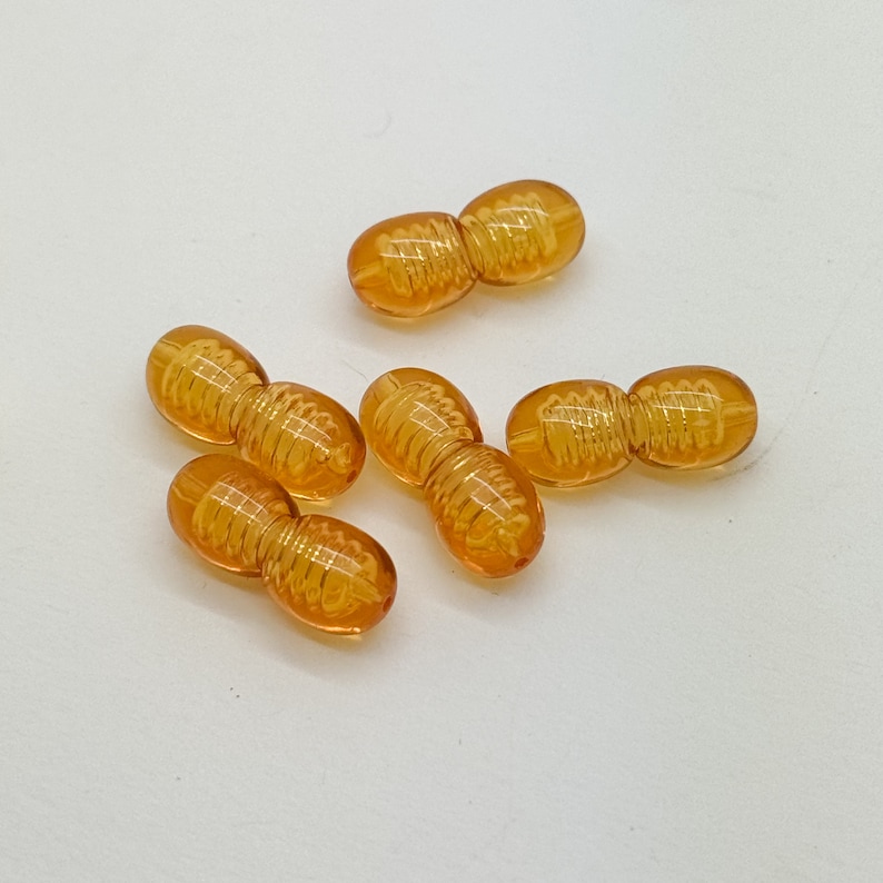May include: Six amber-colored glass beads with a swirl design. The beads are connected in pairs.