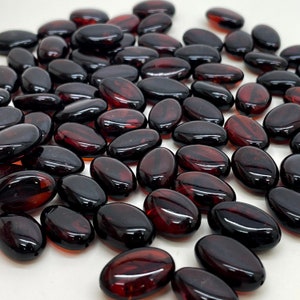 Può includere: Un grande gruppo di perline di vetro ovali di colore rosso scuro. Le perline sono lisce e lucide.